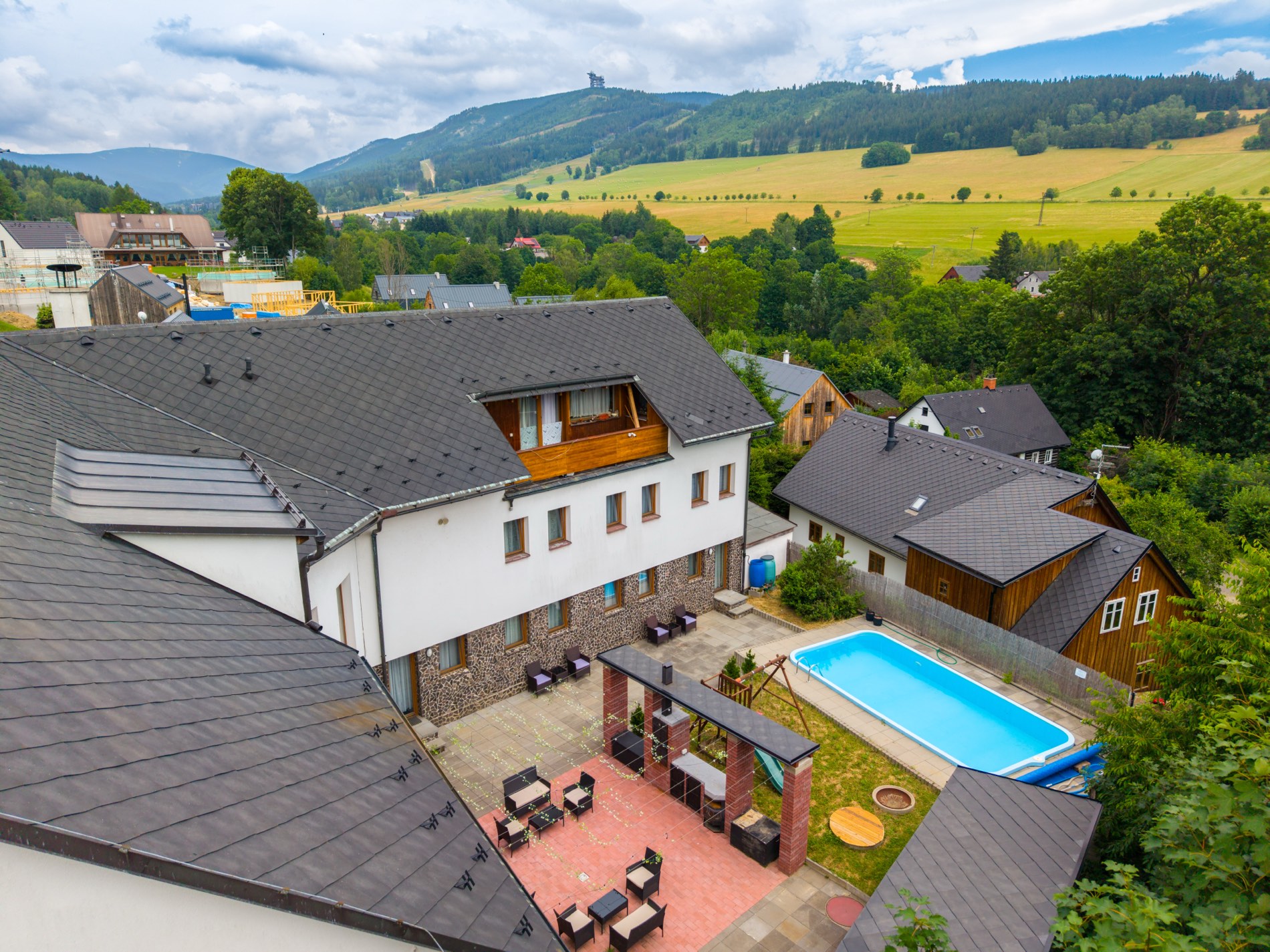 Penzion Valevil z dronu: dvůr s bazénem a terasou, v pozadí sjezdovky Dolní Moravy a Stezka v oblacích